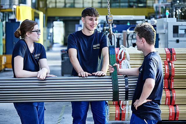 Drei Azubis von heinrichs drehteile stehen an Stahlrohren
